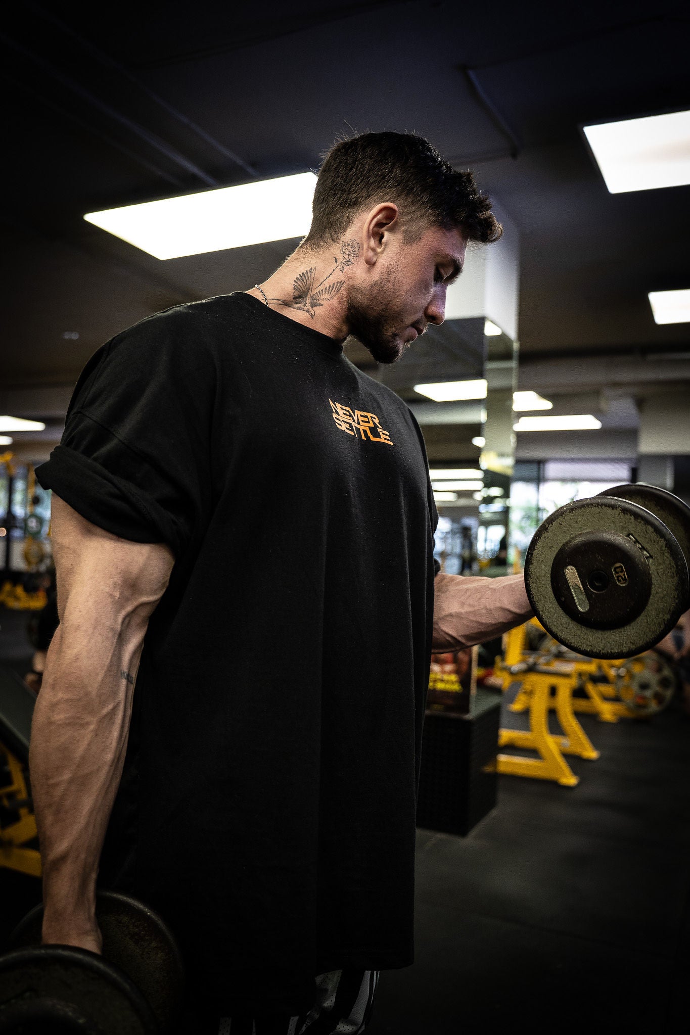 Man lifting a dumbbell in a gym setting wearing a NEVER SETTLE Tee shirt | Trusted by Australian athletes – Shop now at Strom Sports Australia.
